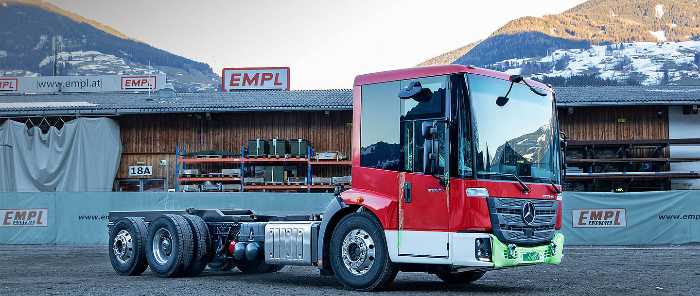 Das Chassis eines Econic 2635 steht auf dem Hof des Spezialaufrüststellers EMPL, im Hintergrund ist die Kulisse der österreichischen Alpen zu sehen.